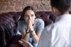 Young woman sat on couch looking pensive whilst talking to someone