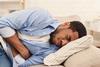 Man lying on bed clutching stomach in pain