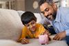 Father and son playing with piggy bank on sofa