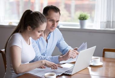 Couple sat at a table looking at a laptop making notes