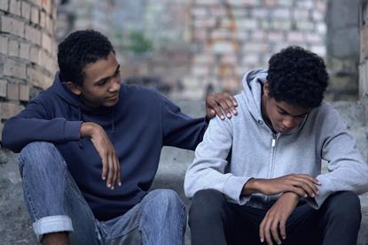 Young man sat with a friend with a comforting hand on his shoulder