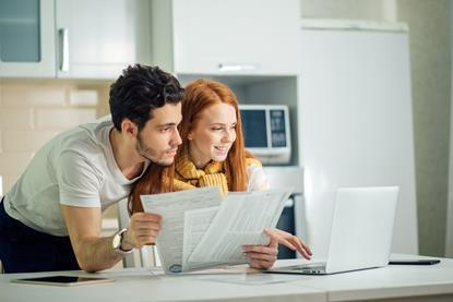COuple looking at a laptop in their home whilst sifting through paperwork