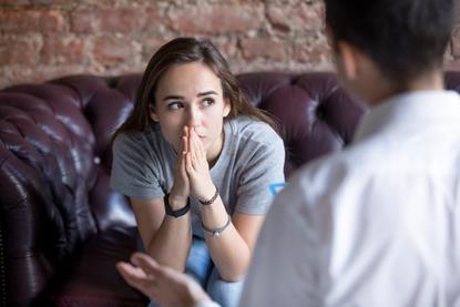 Young woman sat on couch looking pensive whilst talking to someone