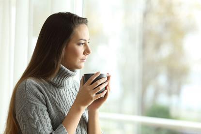 Woman holding a cup of tea staring out of a window