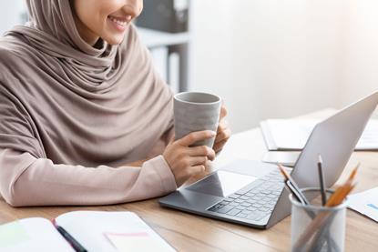 Woman sat at laptop holding a coffee