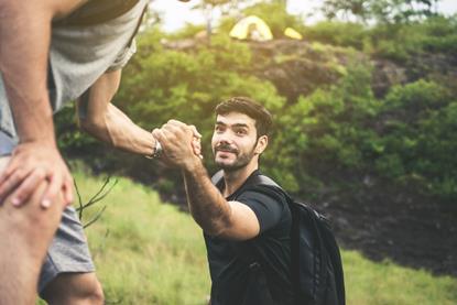 Man giving a friend a helping hand up a hill