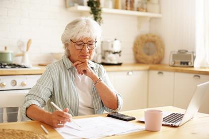 Older lady sat at kitchen table with laptop paperwork and calculator