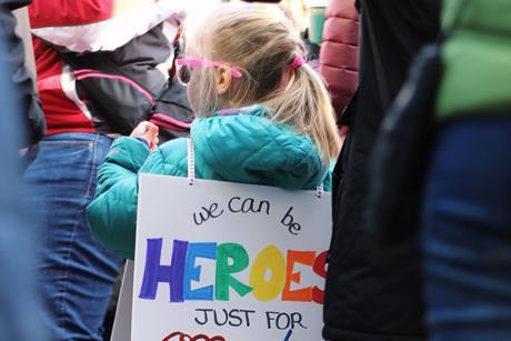 Child carrying rainbow we can be heroes sign