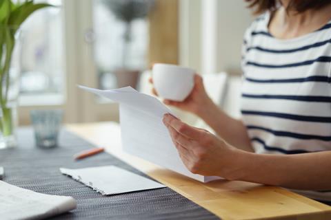 Person sat at a table looking at paperwork drinking a coffee